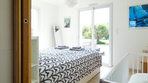 Un dormitorio con una cama, una cuna blanca, un ventanal grande y una puerta que da al exterior.