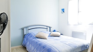 A bedroom with a bed, pillows, a fan, and a window. - Quiet house near the ocean, Les Sables 6 people (Les Sables-d´Olonne)