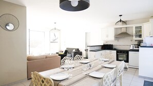 A modern kitchen with white cabinets, a dining area with a long table set for six, and a living area with a sofa and chairs. - Quiet house near the ocean, Les Sables 6 people (Les Sables-d´Olonne)