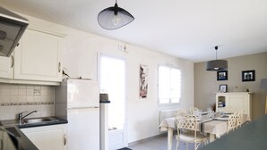 A kitchen with white cabinets, a refrigerator, a sink, and a dining area with a table and chairs. - Quiet house near the ocean, Les Sables 6 people (Les Sables-d´Olonne)