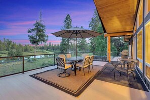 Een balkon met een tafel en stoelen, een grote parasol en uitzicht op bomen en een waterpartij.