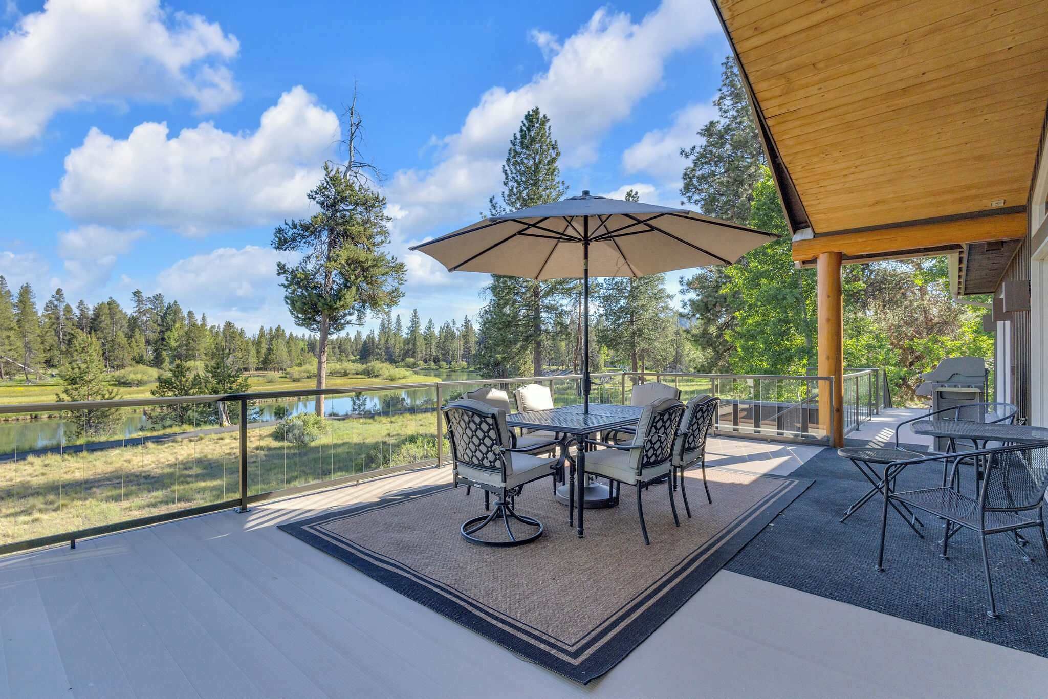 Eine überdachte Terrasse im Freien mit Tisch und Stühlen, mit Blick auf einen See und Wald.