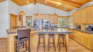 Une cuisine spacieuse avec des meubles en bois, un grand îlot central doté de tabourets et un éclairage suspendu.