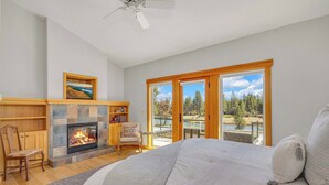 Une chambre avec une cheminée, un grand lit, un fauteuil et une vue sur un lac et une forêt, visible à travers les portes-fenêtres coulissantes.