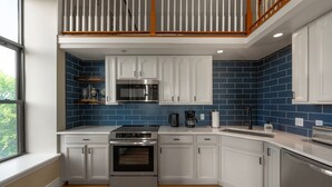 A modern kitchen with white cabinets, blue tiles, stainless steel appliances, and a wooden staircase.