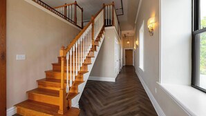 A wooden staircase with white balusters leading to a landing, flanked by light-colored walls and a window with a view.