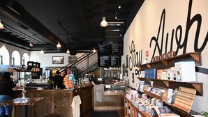 A café interior with a menu board, wooden furniture, and a staircase leading to an upper level.