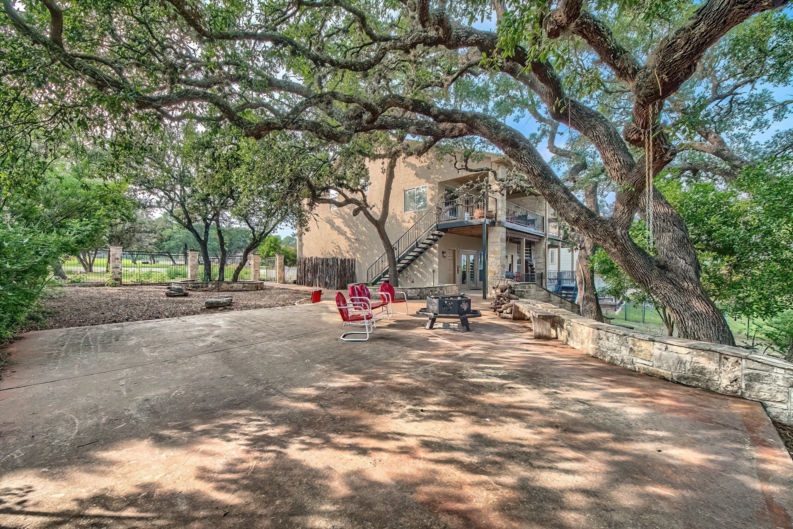 A courtyard with a large tree, a stone wall, and a building with a balcony.