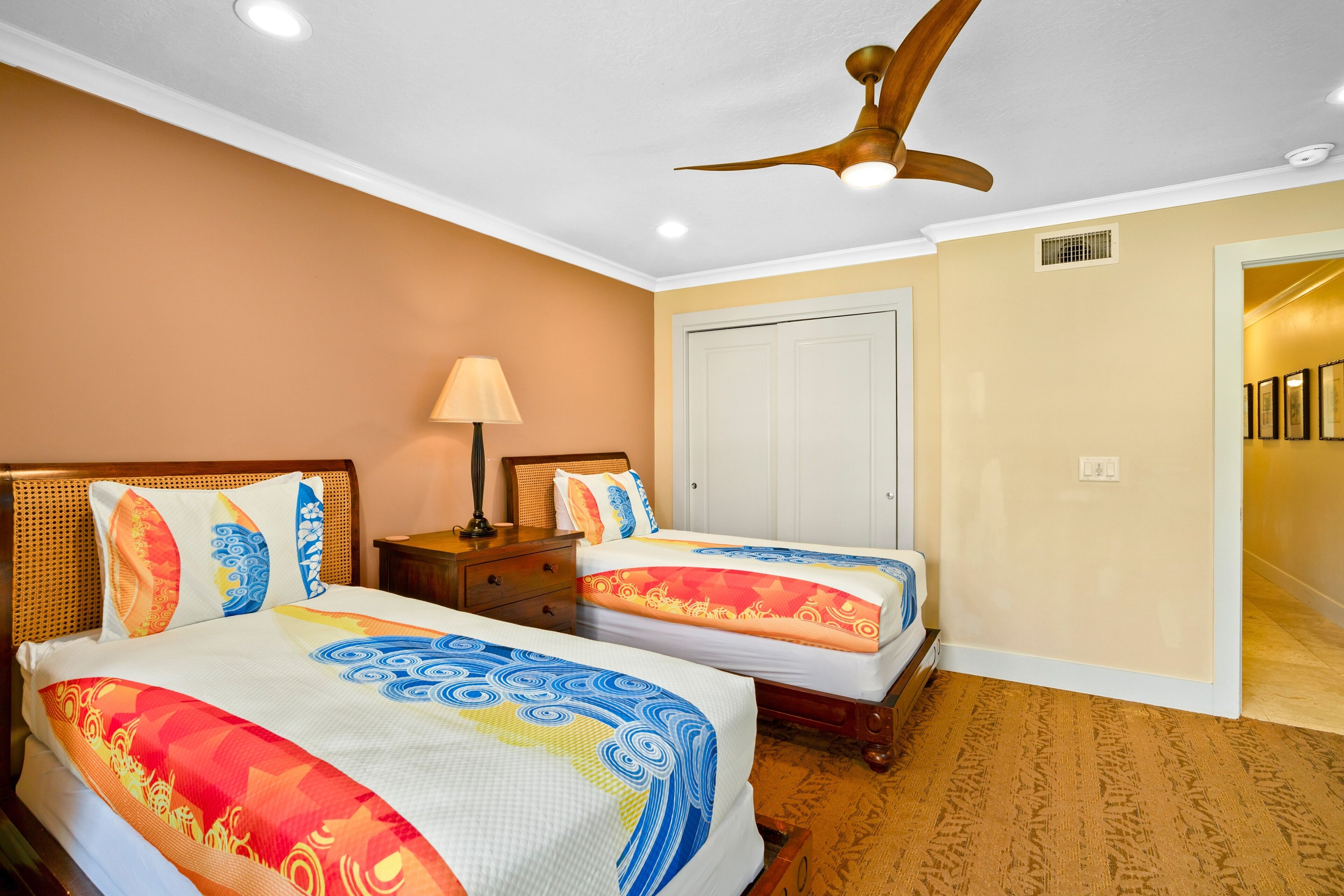 A hotel room with two beds, a ceiling fan, a nightstand, and a door leading to another room.