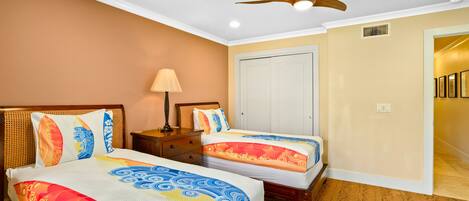 A hotel room with two beds, a ceiling fan, a nightstand, and a door leading to another room.