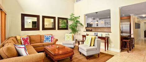 A spacious living room with a large sectional sofa, a coffee table, and a dining area with a kitchen in the background.