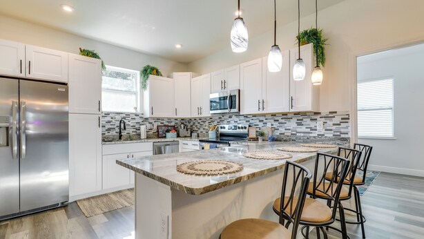 Una cocina moderna con armarios blancos, un refrigerador de acero inoxidable, un microondas y una isla grande con taburetes de bar.