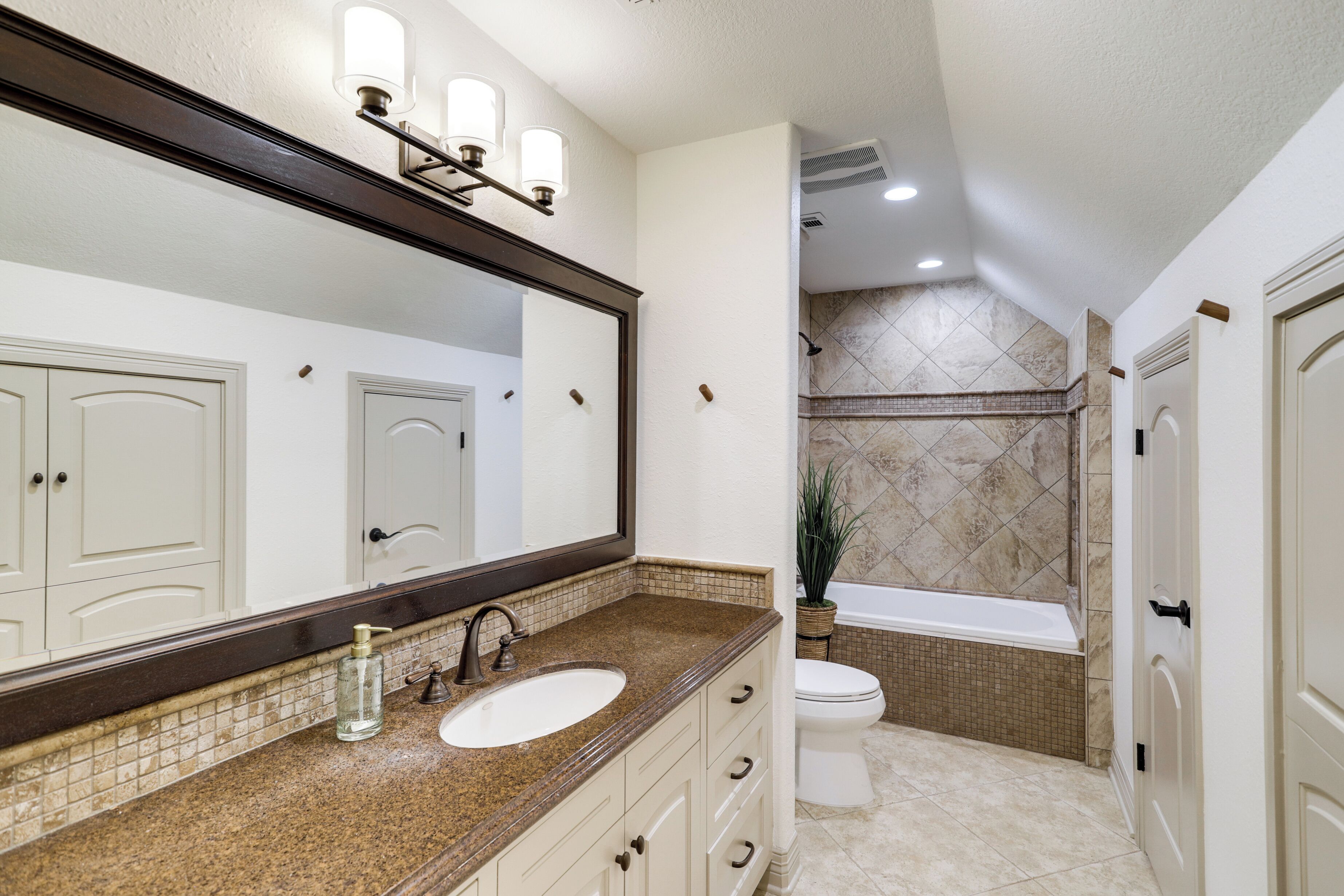 A bathroom with a large mirror, a sink, a toilet, and a bathtub.