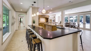A modern kitchen with a large island, bar stools, pendant lighting, and a view of the outdoors. - Private 25 Acre Estate w/ Lake: Fish & Canoe! (Houston)