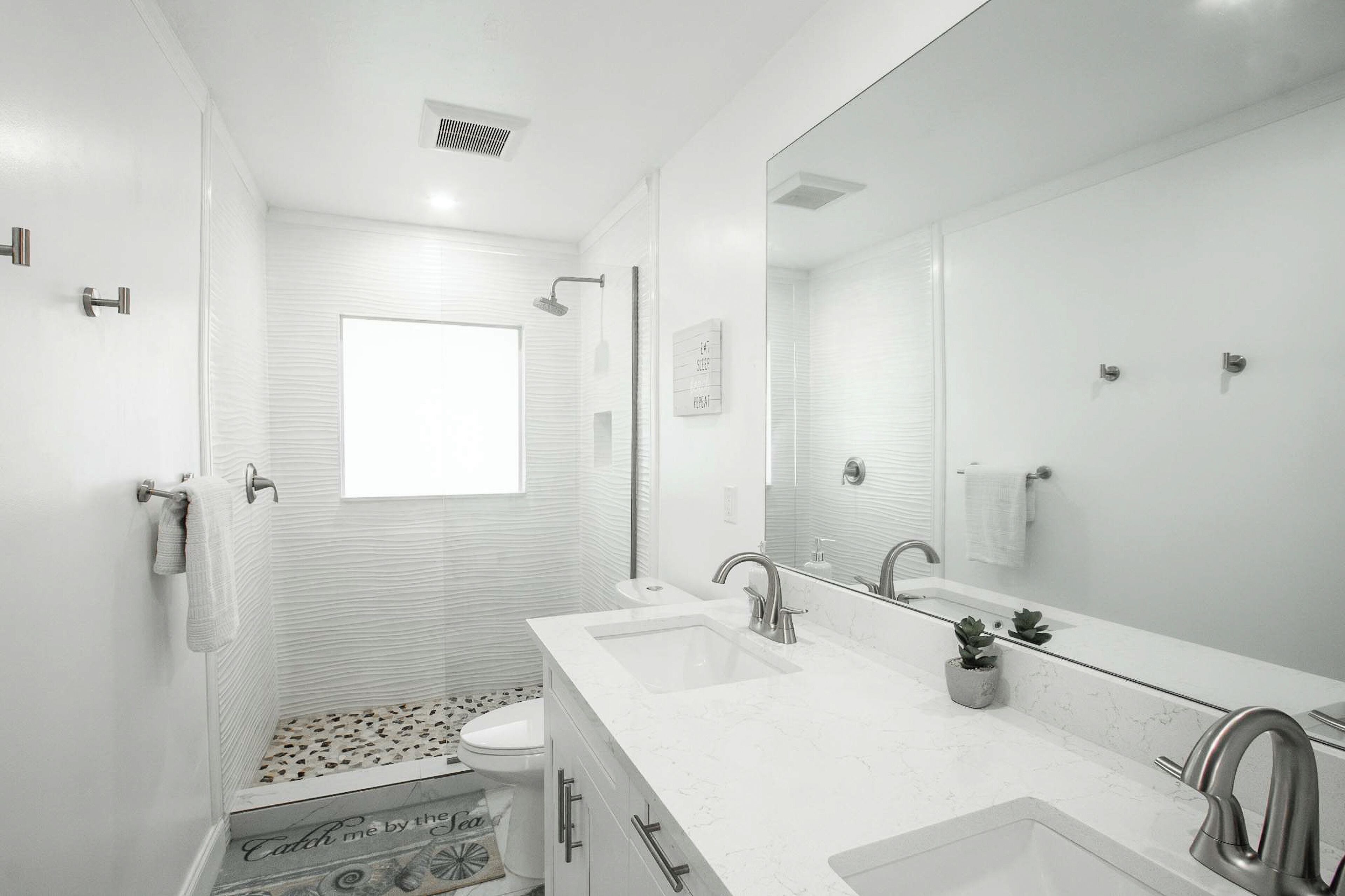 A modern bathroom with a large mirror, two sinks, and a shower.