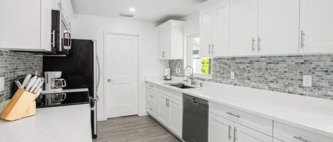 A modern kitchen with white cabinets, a black countertop, and a backsplash with gray tiles.