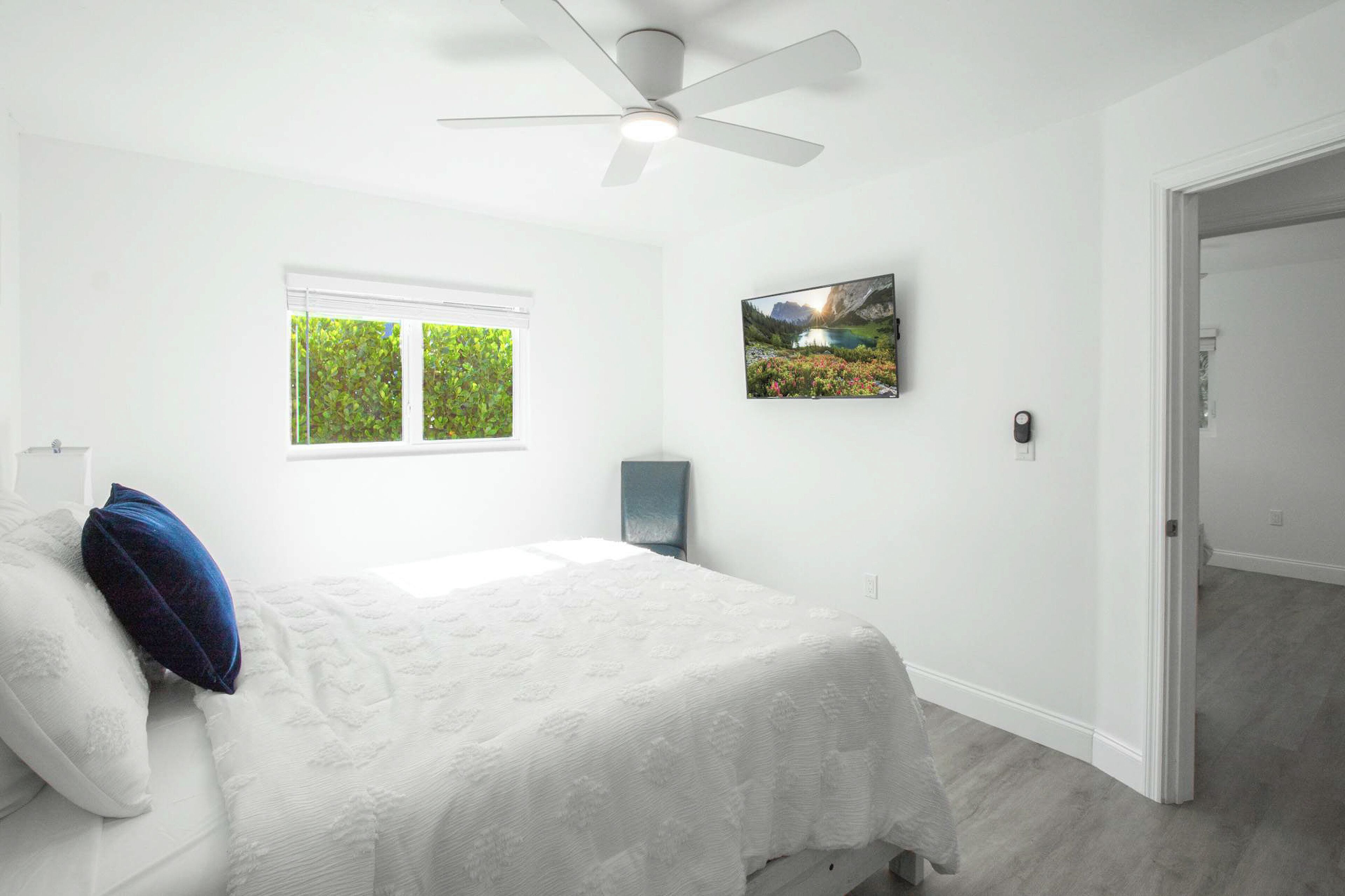 Un dormitorio con cama, ventilador de techo, ventana con persianas y un cuadro en la pared.