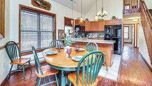A dining area with a wooden table and chairs, a ceiling fan, and a kitchen in the background. - Serene Poconos Cabin w/ Hot Tub & Beach Access! (Albrightsville)
