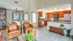 A spacious living room with leather chairs, a coffee table, and a bookshelf. The kitchen features wooden cabinets, a microwave, and a refrigerator.