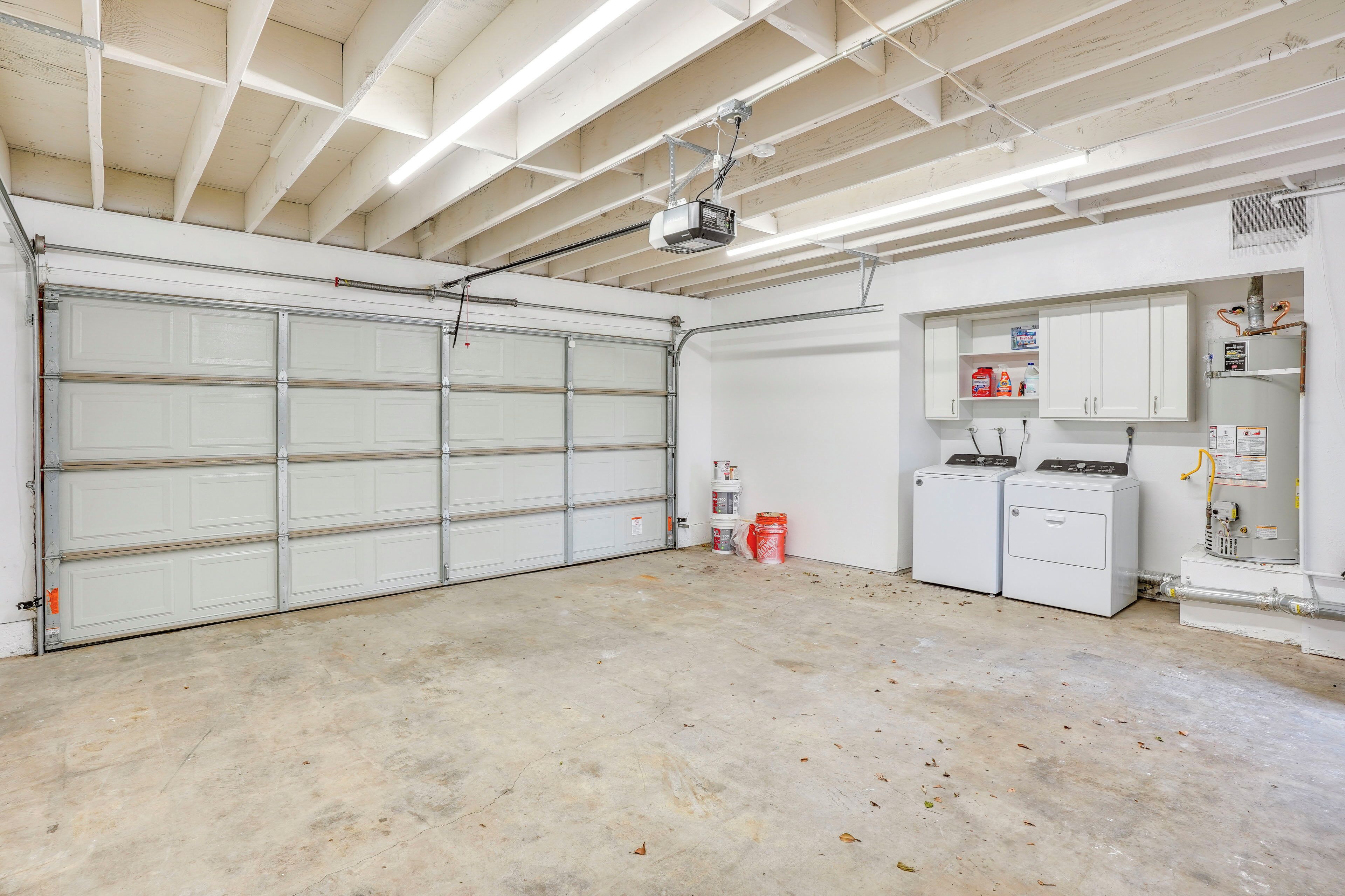 Een ruime garage met een grote witte garagepoort, een projector aan het plafond en twee witte wasmachines.
