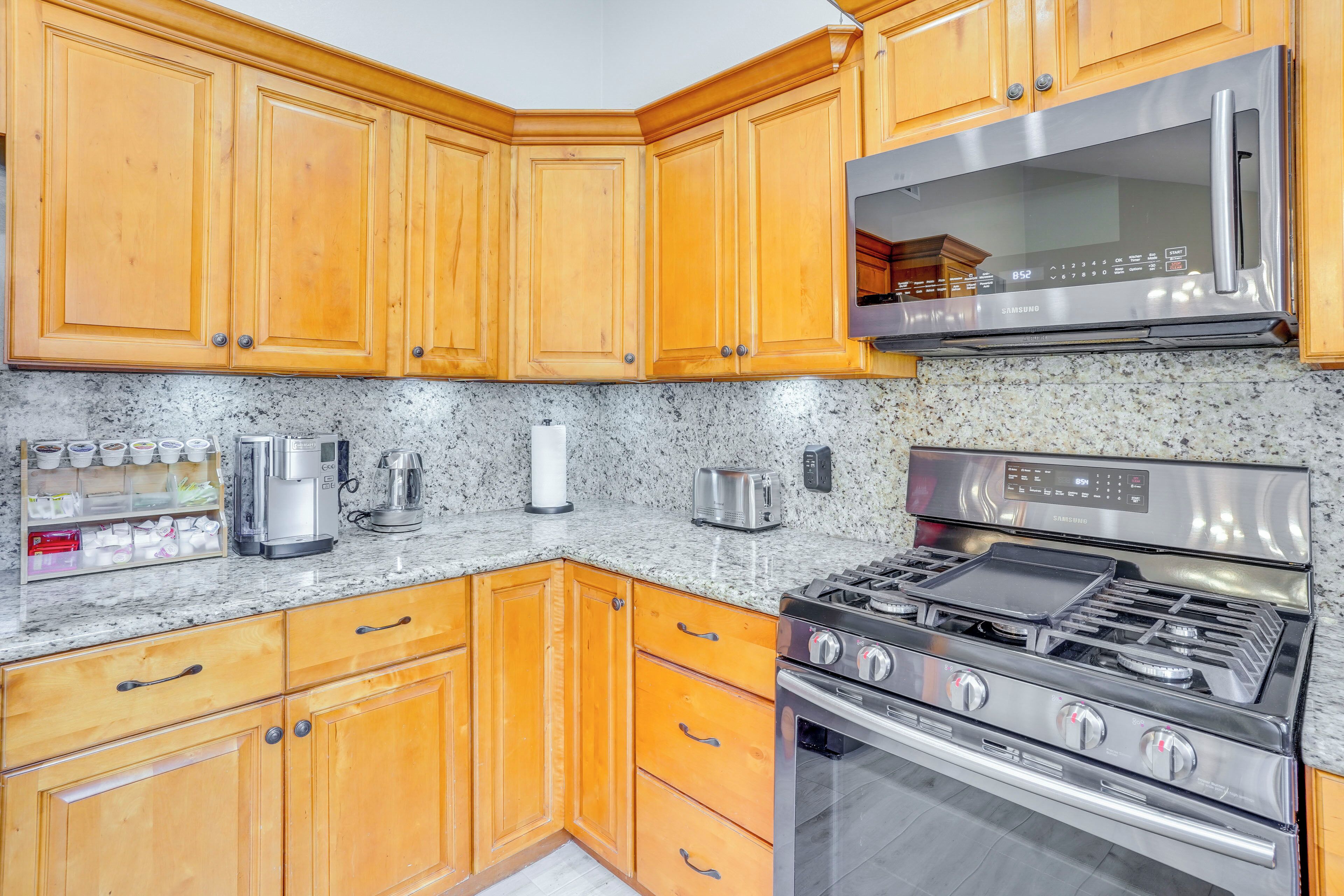A kitchen with wooden cabinets, a stainless steel microwave, a gas stove, and granite countertops.