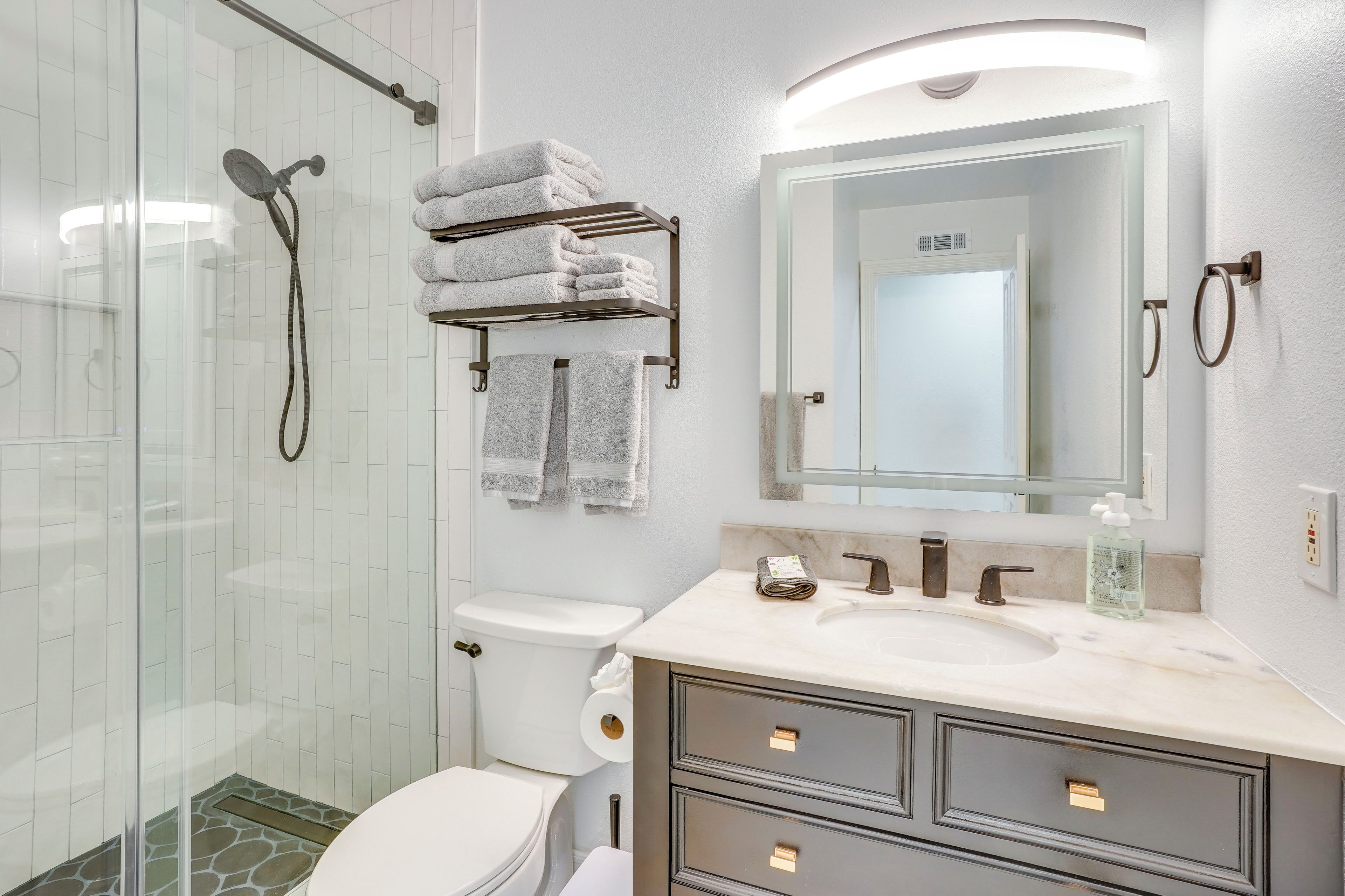 Ett modernt badrum med en duschkabin i glas, en toalett, ett handfat med en bänkskiva i marmor och en spegel med en handdukshängare ovanför.