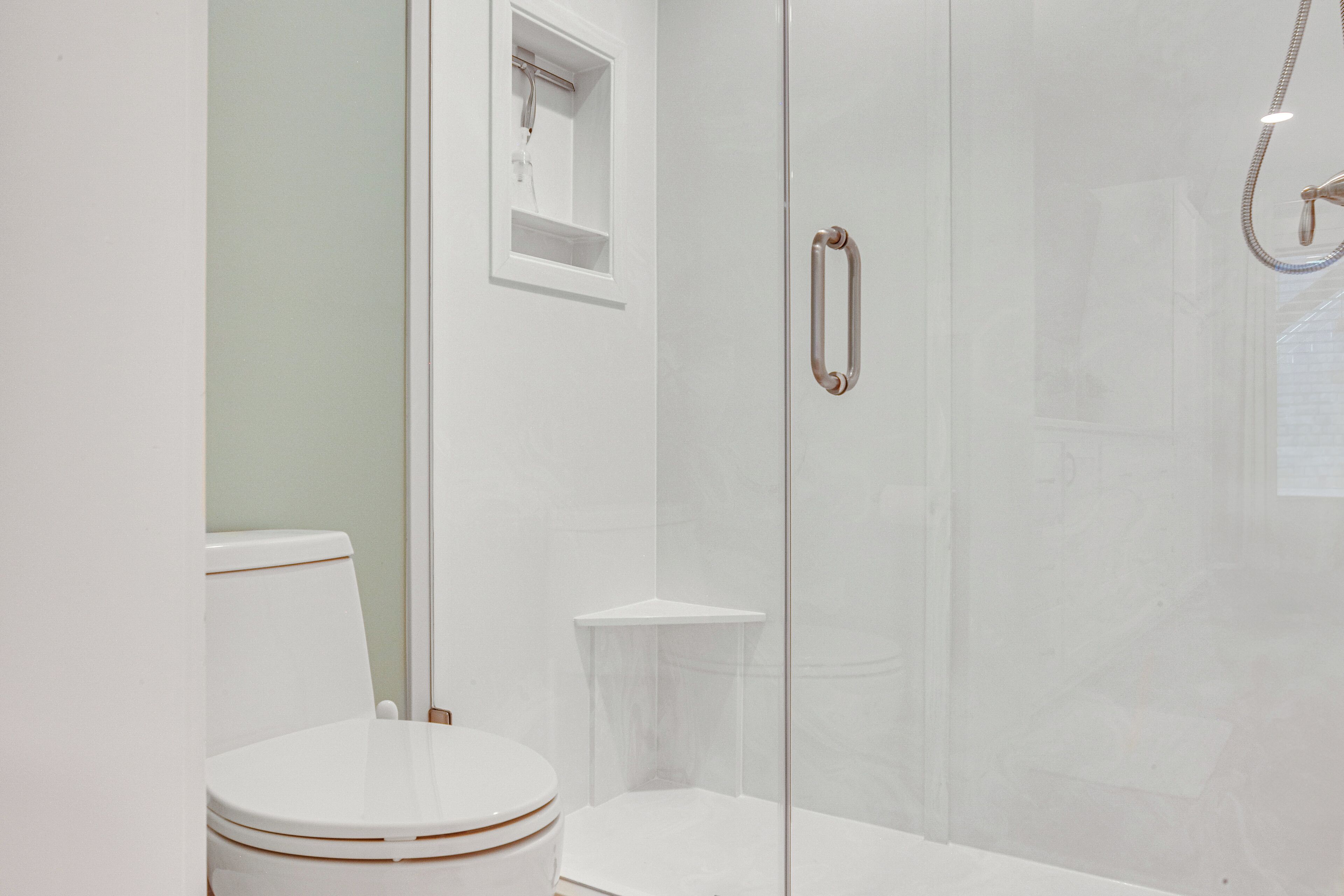 A modern bathroom with a glass-enclosed shower, a white toilet, and a small shelf.