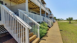 A wooden deck leading to a row of white buildings with balconies.