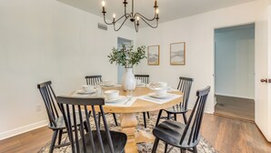 A dining room with a round table, black chairs, a chandelier, a vase with plants, and framed pictures on the wall. - Family-friendly Home: 6 Mi to Downtown Mobile! (Mobile)