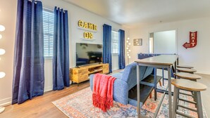 A modern living room with a TV, blue curtains, a red throw, and a wooden coffee table. - Family-friendly Home: 6 Mi to Downtown Mobile! (Mobile)