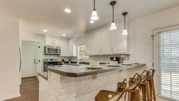 A kitchen with white cabinets, a granite countertop, a microwave, and a sink. There are three pendant lights hanging above the island. - Family-friendly Home: 6 Mi to Downtown Mobile! (Mobile)