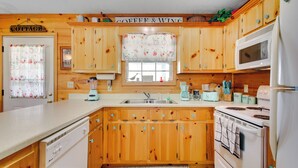 A kitchen with wooden cabinets, a white refrigerator, a microwave, a stove, and a coffee maker. - Cozy Cabin w/ Grill & Fire Pit By Dale Hollow Lake (Byrdstown)