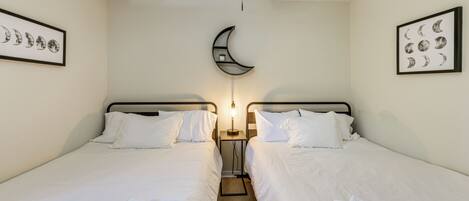 Quarto de hotel com duas camas, ventoinha no teto, decoração em formato de crescente lunar na parede e quadros com as fases da lua.