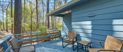 A wooden deck with wicker chairs and a table, overlooking a forested area.
