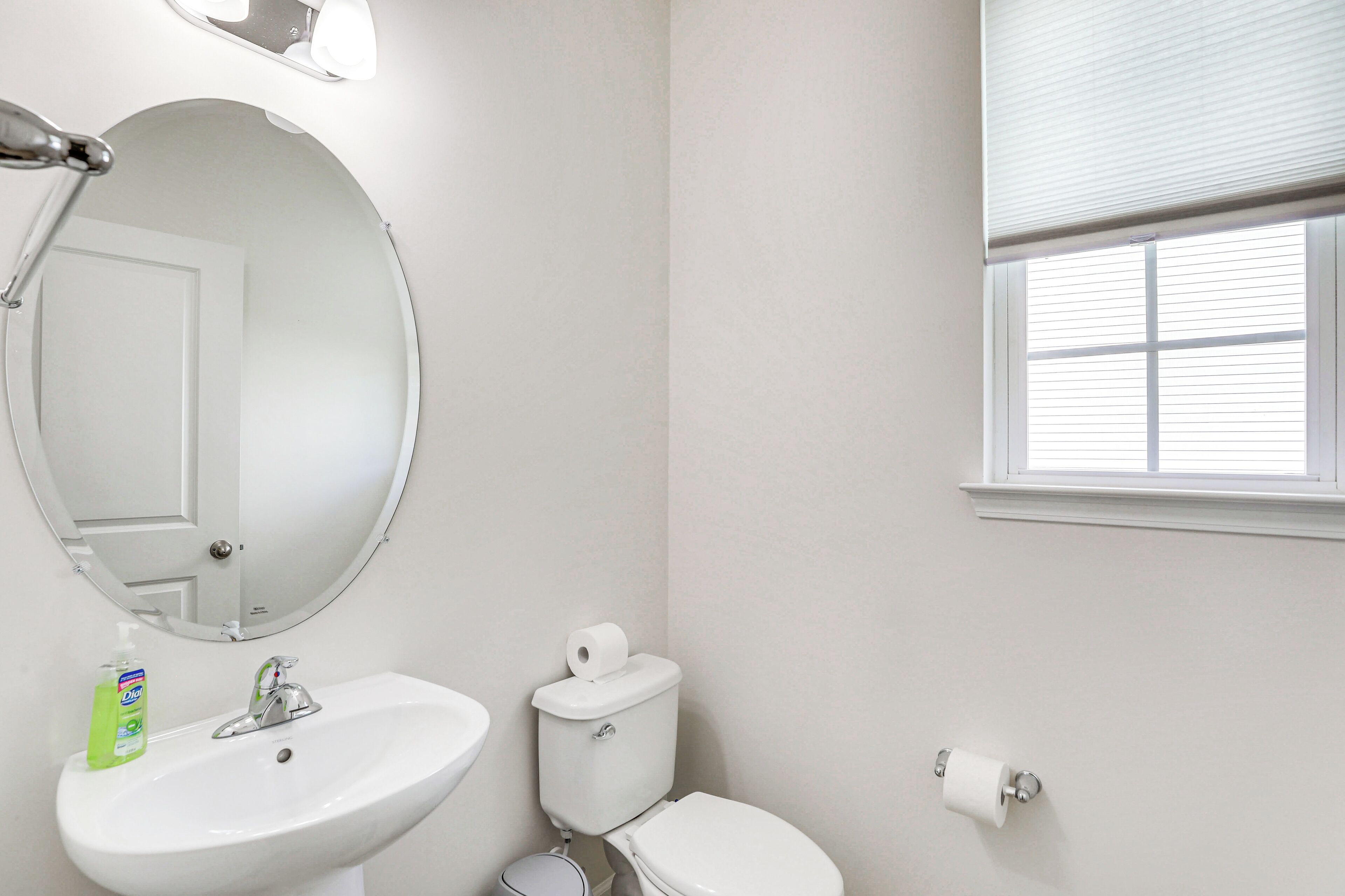 Un baño con lavamanos, espejo, inodoro y ventana.
