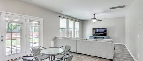 A spacious living area with a sofa, a dining table with chairs, a television, and a ceiling fan.