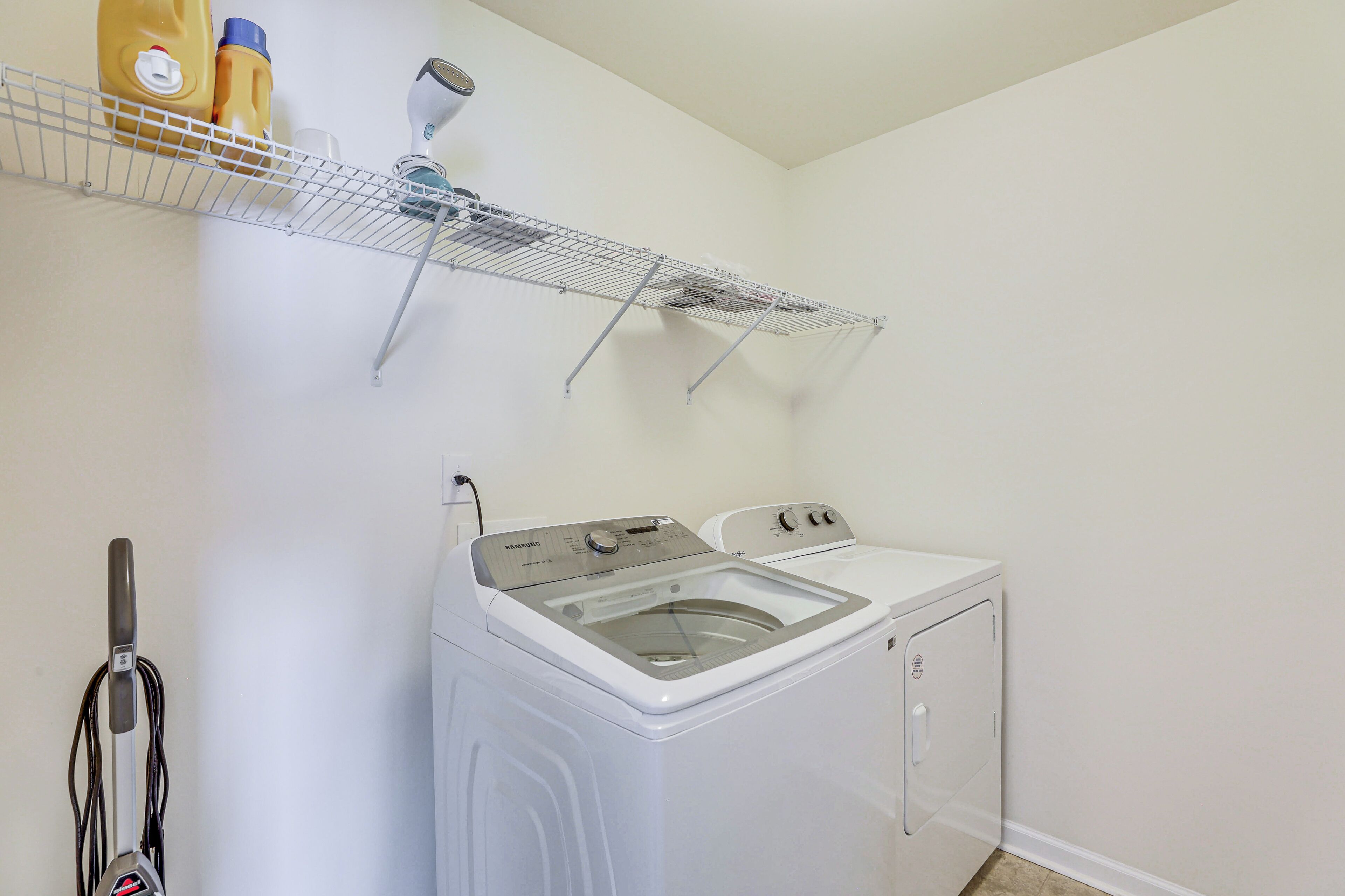 A laundry area with a washing machine, a drying rack, and a vacuum cleaner.