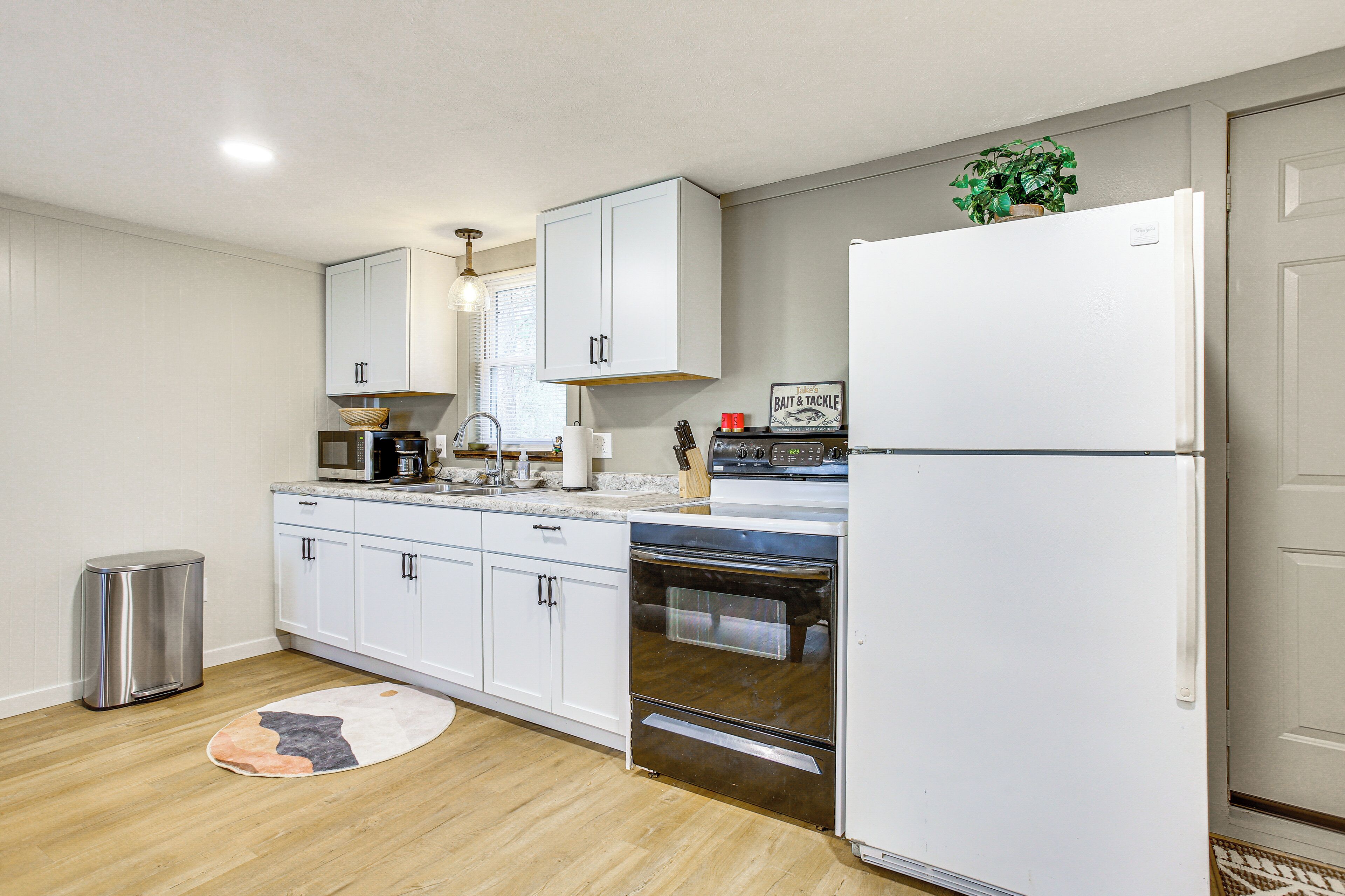 Una cocina moderna con armarios blancos, un cubo de basura de acero inoxidable, un microondas, un horno y un refrigerador.