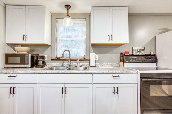 A kitchen with white cabinets, a stainless steel sink, a microwave, a coffee maker, and a stove.
