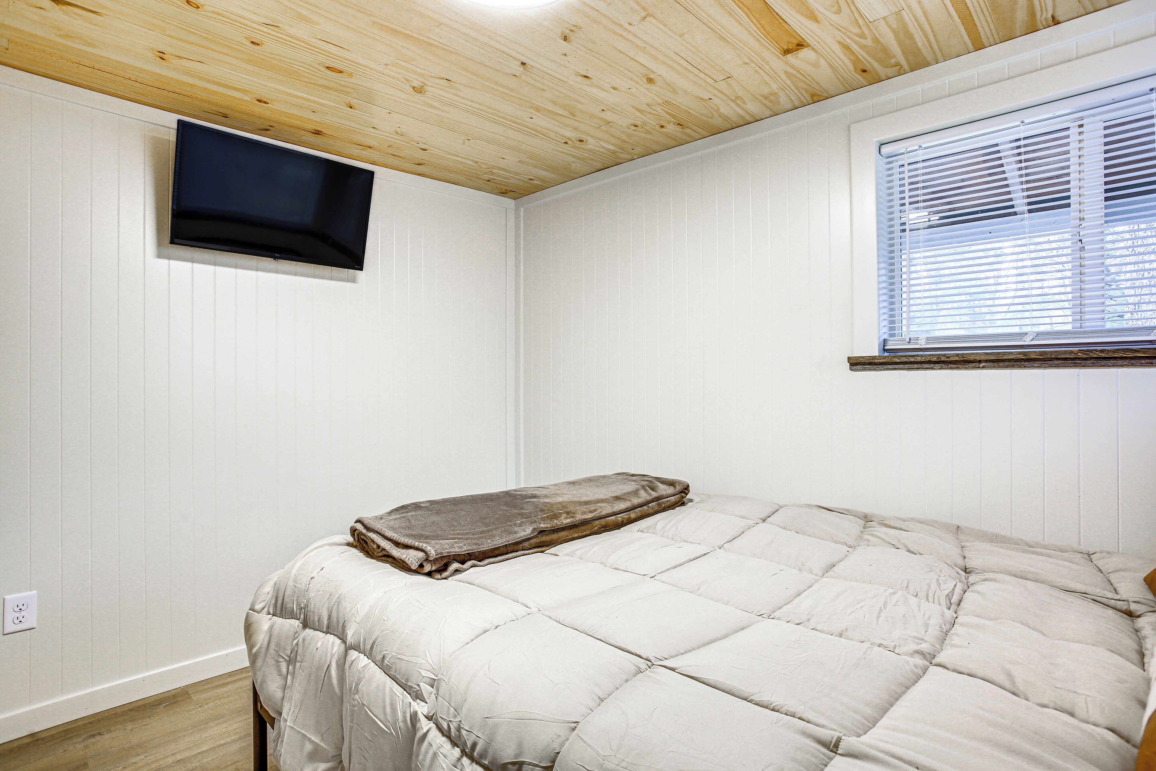 Una camera da letto con un letto, soffitto in legno, una finestra con persiane e televisore a parete.