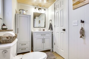 A bathroom with a white toilet, a white sink with a mirror above it, and a white cabinet with drawers. - Updated Wellston Cabin, Walk to Lake Beach + Dock! (Wellston)