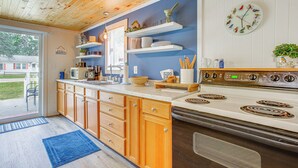 A kitchen with wooden cabinets, a white stove, and blue walls. - Cozy Wellston Cabin - Walk to Crystal Lake! (Wellston)