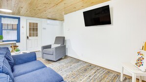 A living room with a blue sofa, a grey armchair, a patterned rug, and a TV mounted on the wall. - Cozy Wellston Cabin - Walk to Crystal Lake! (Wellston)