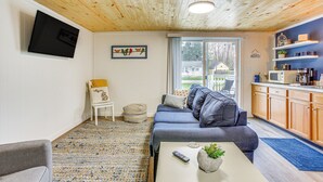 A cozy living room with a sofa, a small table with a plant, and a TV mounted on the wall. - Cozy Wellston Cabin - Walk to Crystal Lake! (Wellston)