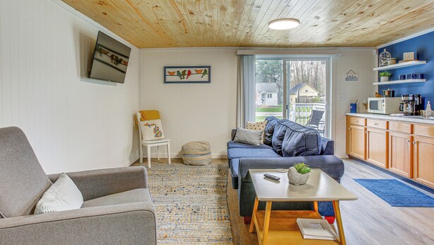 A living room with a grey sofa, a blue sofa, a wooden coffee table, and a television mounted on the wall. - Cozy Wellston Cabin - Walk to Crystal Lake! (Wellston)