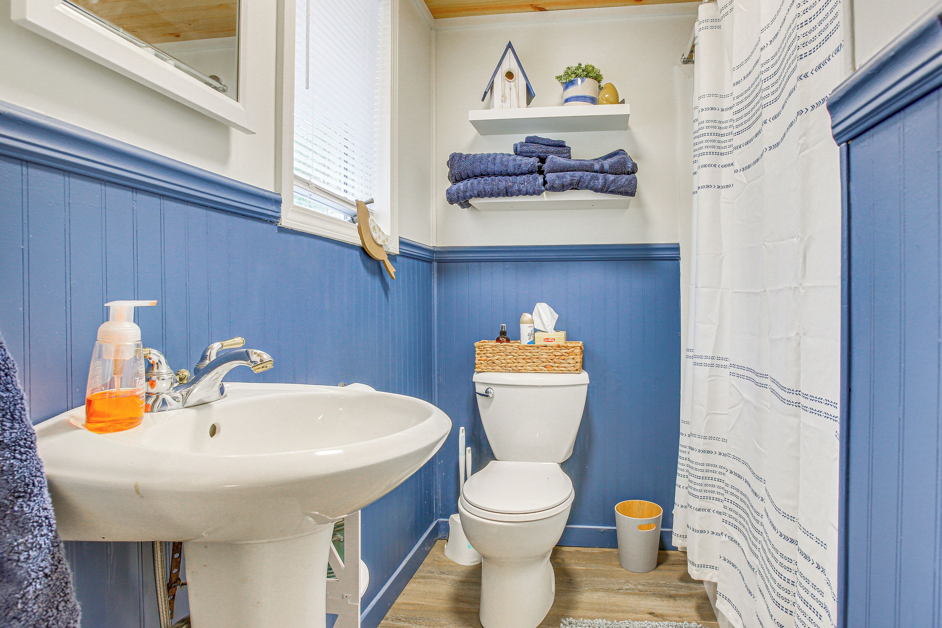 Un baño con un lavabo blanco, un inodoro blanco, una cortina de ducha azul y suelo de madera.
