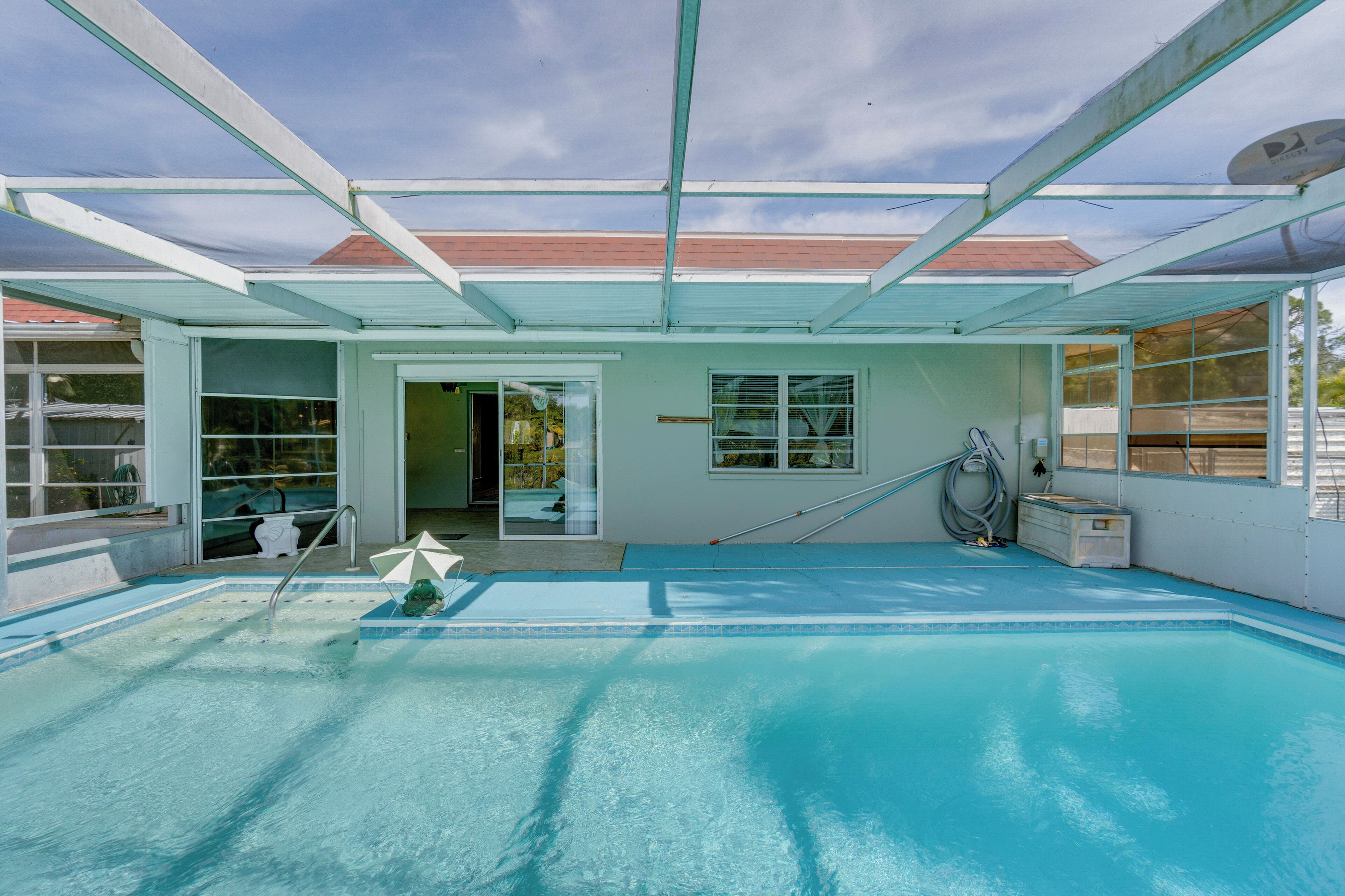 A covered swimming pool with a glass ceiling, a poolside umbrella, and a hose for filling the pool.