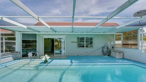 Una piscina cubierta con techo de cristal, una sombrilla junto a la piscina y una manguera para llenarla.