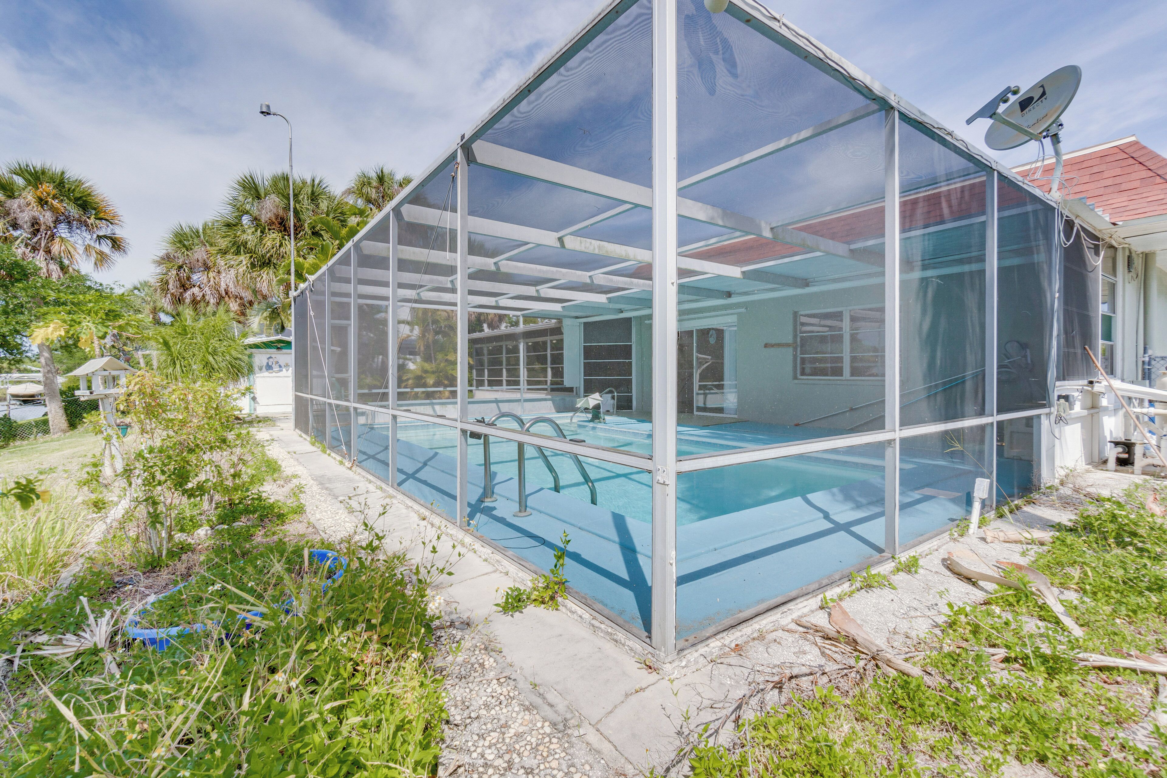 Une piscine intérieure, entourée de verdure et dotée d’une structure métallique, avec une maison visible au loin.