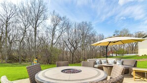 A circular outdoor seating area with wicker furniture and a fire pit, surrounded by a lawn and trees. - Rock Island Home w/ Private Yard & Fire Pit Table! (Rock Island)